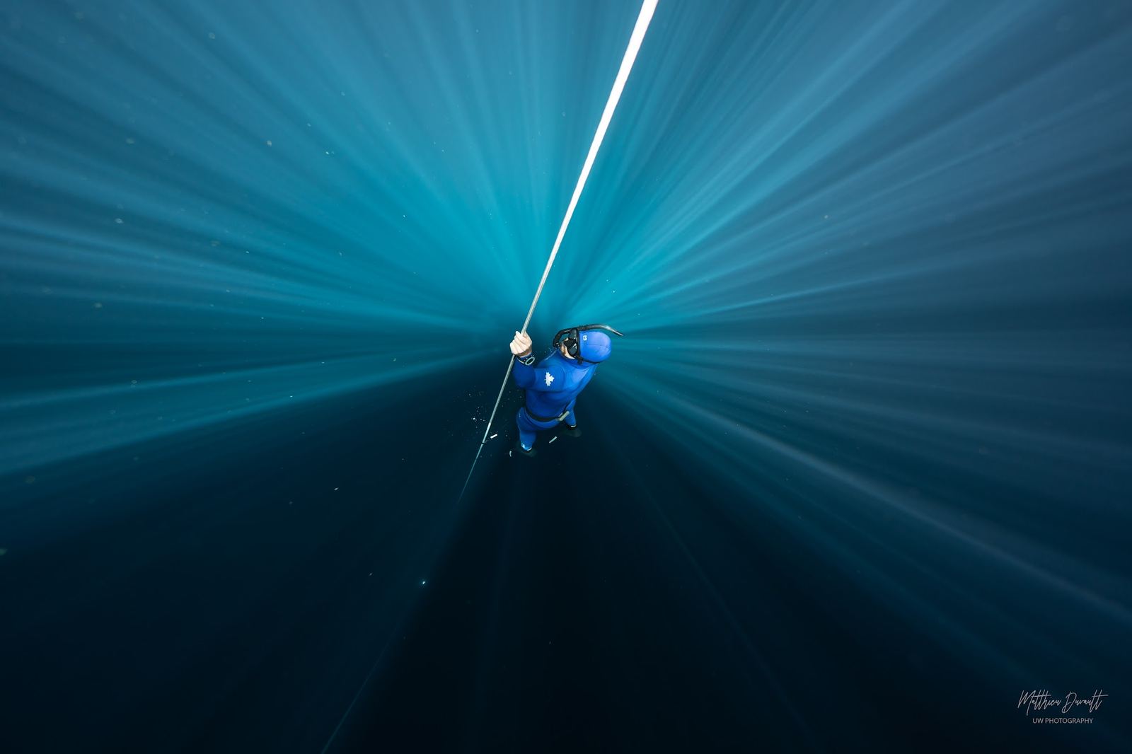 A freediver in deep blue water with shafts of light streaming down